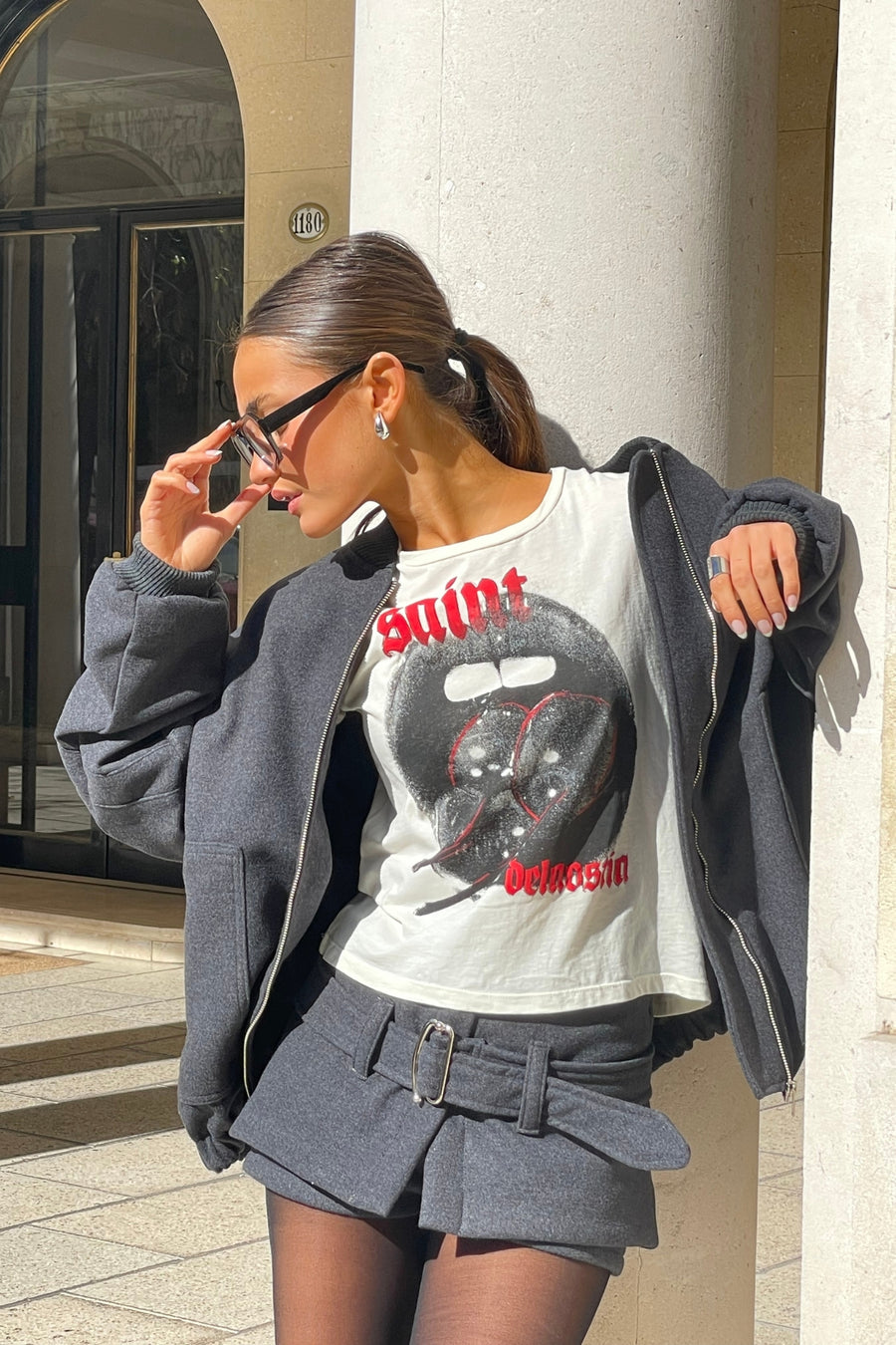 Mujer joven posando con anteojos y Short pollera Circe tiro bajo de paño con cinturón color gris oscuro.