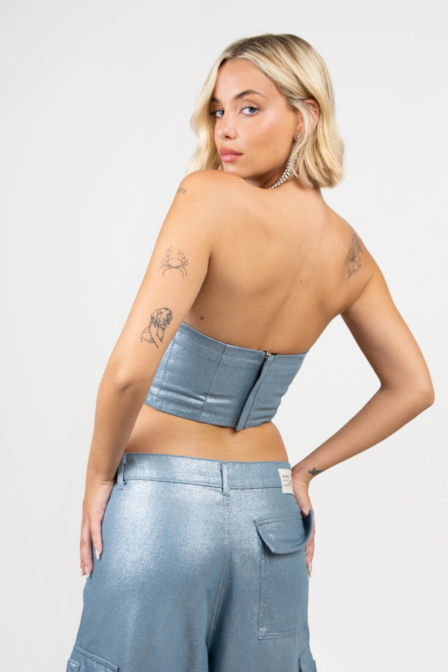 Modelo posando de espalda con Corset Blade de denim brillante con devoré, recortes y cierre en la espalda, en conjunto con Pantalón Blade.