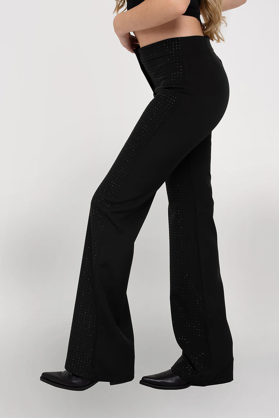 Modelo posando de perfil usando Pantalón Aurora sastrero recto y tiro medio, cuenta con full hotfix en delantero, color negro.