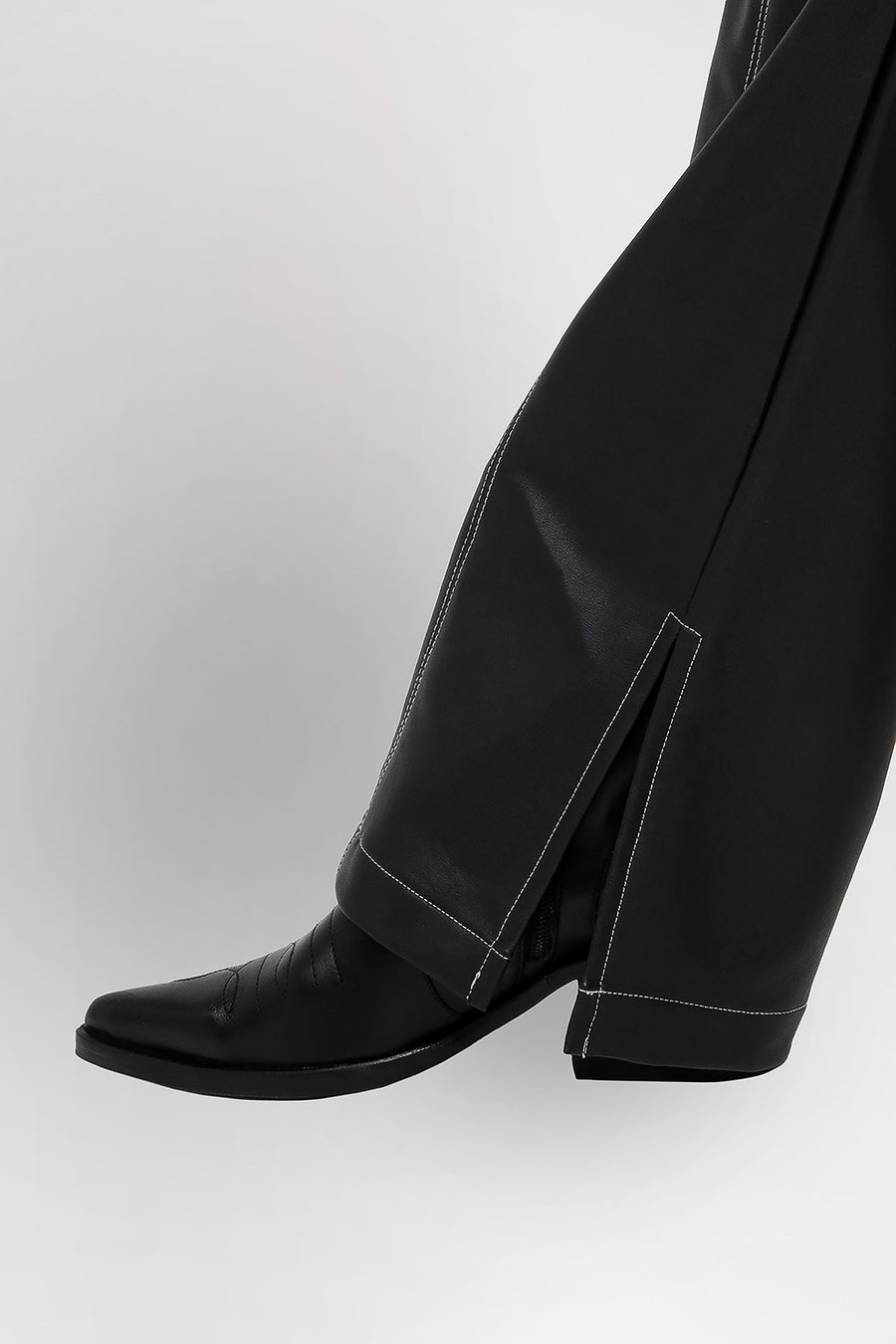 Foto detalle de pierna de modelo usando  Pantalón Shadow de PU, tiro medio. Detalle con pespuntes a contratono y tajo en la botamanga. 