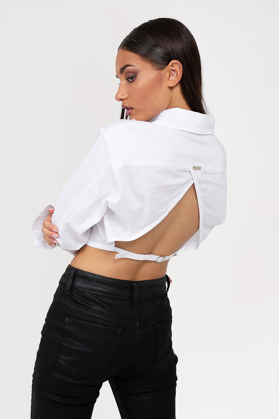 Modelo posando de espalda con Camisa Adrienne crop manga larga con puños Oxford y cuello en punto, espalda descubierta con pasadores para tiras ajustables.