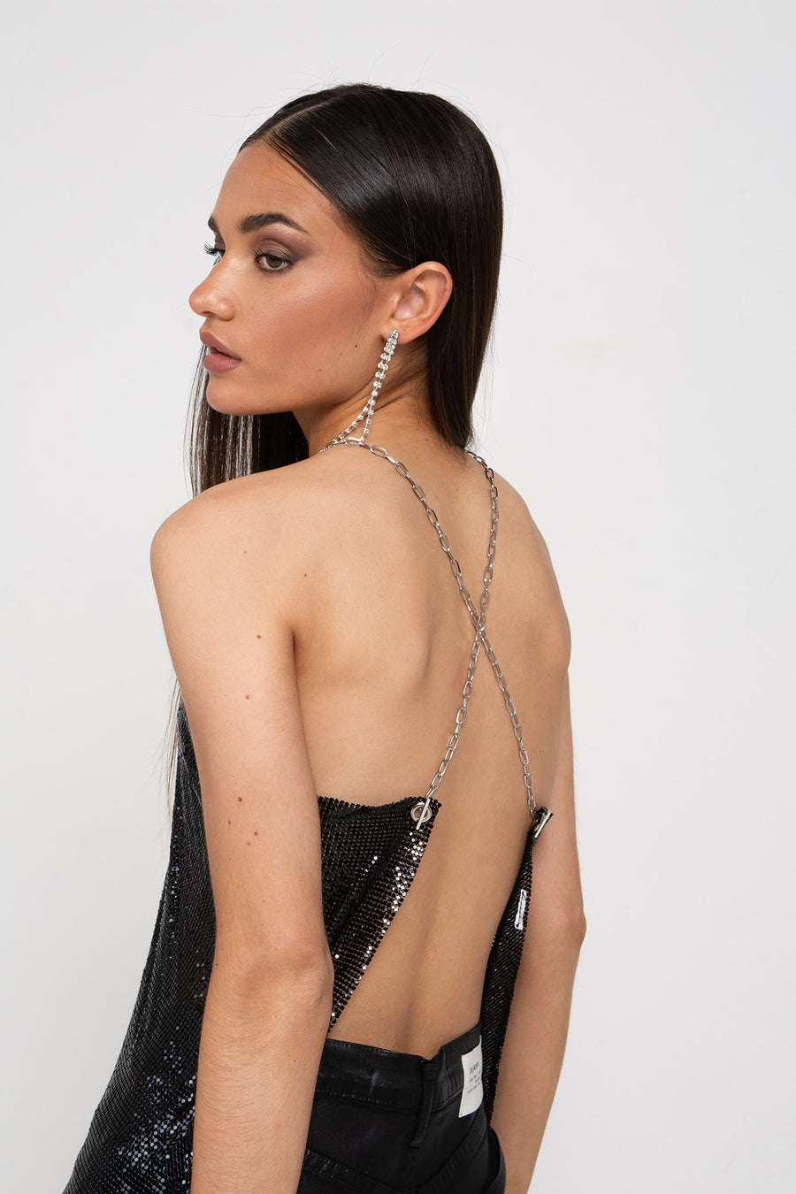 Modelo posando de espaldas con Top Cadell pechera de mallan metálica con argollas y cadenas cruzadas de niquel.