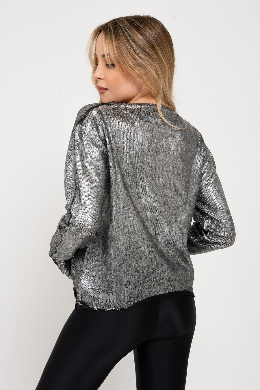 Modelo posando de espalda con Sweater Glam fino de foil plata con cuello redondo. Silueta regular y largo modular hasta la segunda cadera.