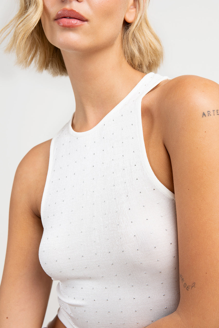 Detalle de modelo posando con Musculosa Martina de jersey con leve brillo y hotfix termoadhesivos en delantero. Largo modular hasta la cintura y silueta slim, color blanco.