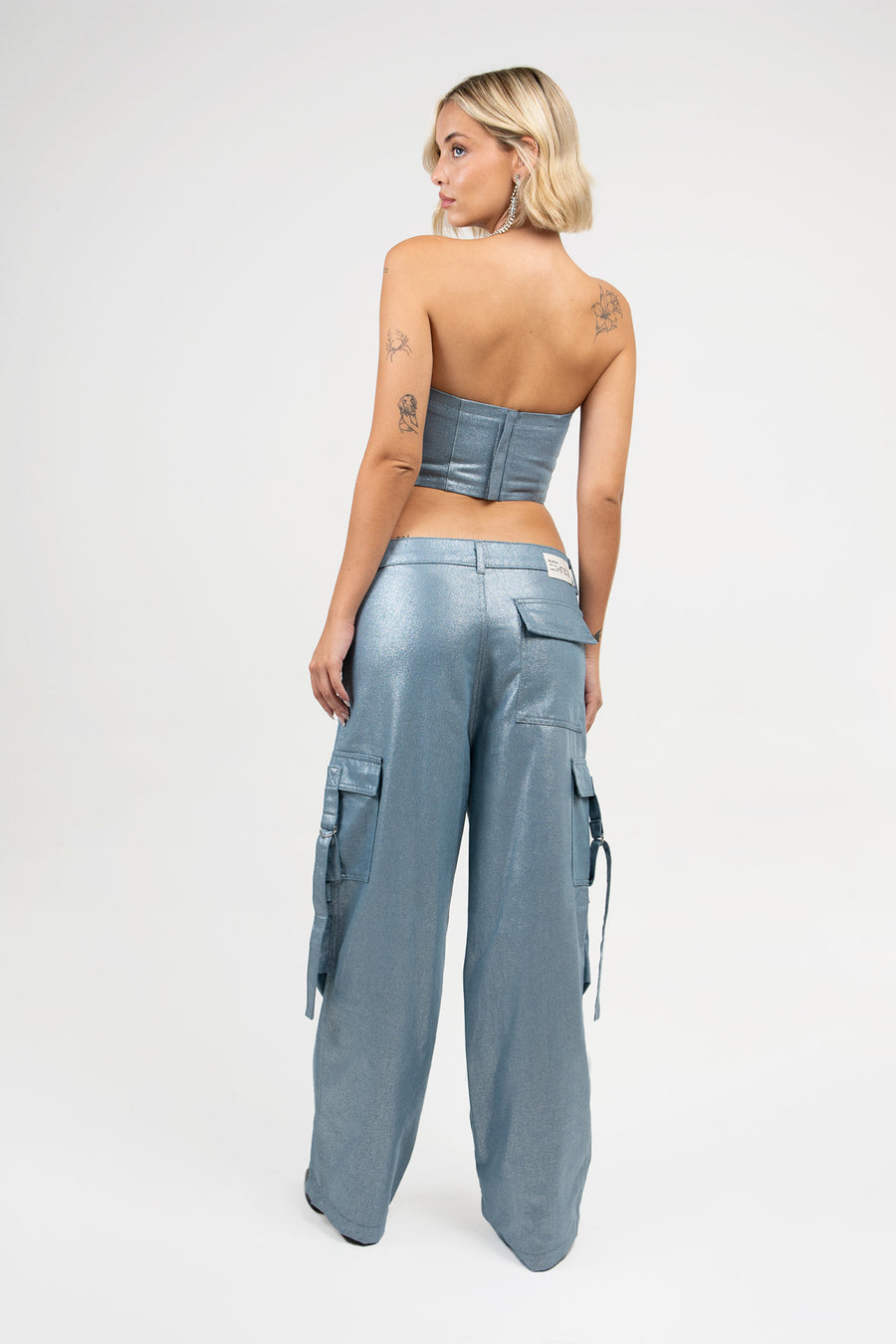 Mujer rubia posando de espaldas con Pantalón Blade de denim con foil, tiro bajo oversize con bolsillos en los laterales, color plata de la marca Delaostia.