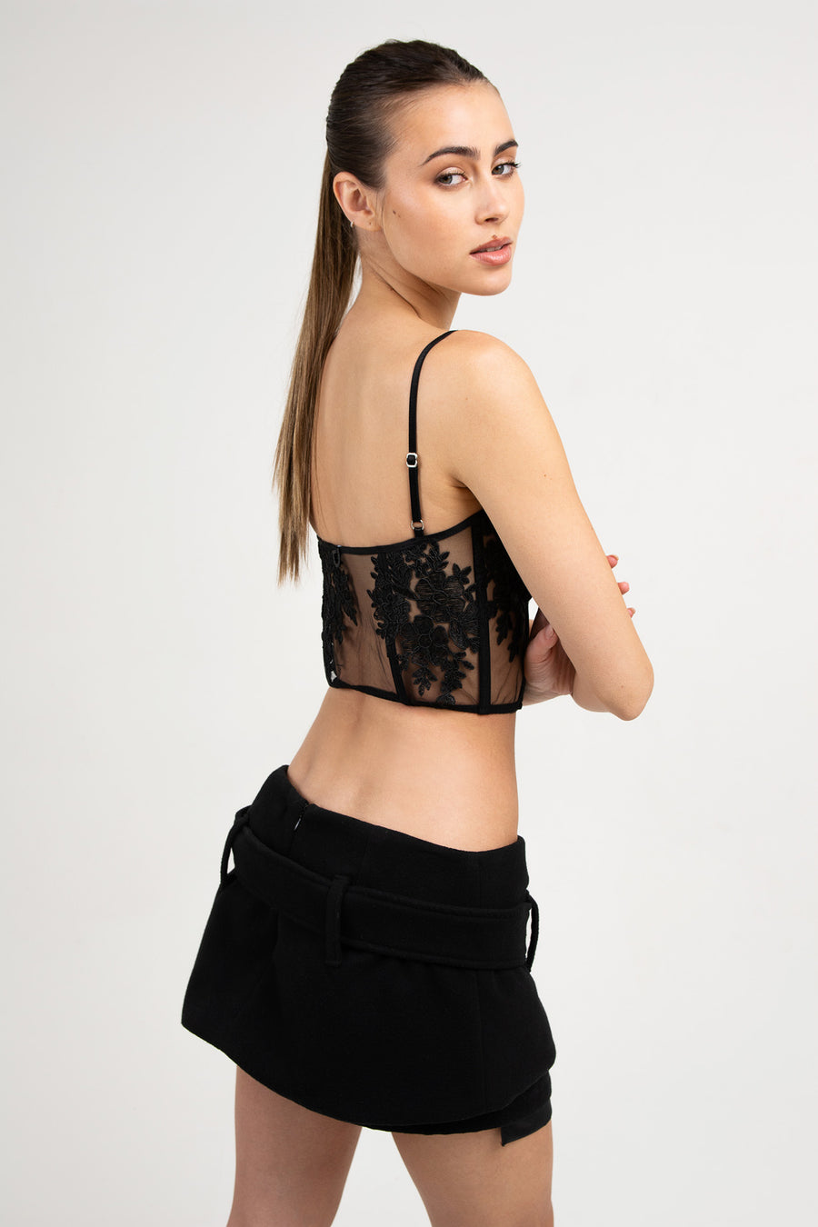 Modelo posando de perfil con Short pollera Circe tiro bajo de paño con cinturón, color negro. 