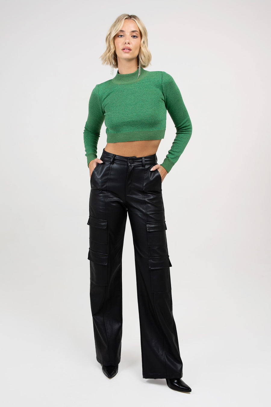 Modelo posando  con las manos en los bolsillos del pantalón y usando el Sweater Zane polera anatómico con brillo color verde. El sweater es corto por debajo de las costillas y al cuerpo.