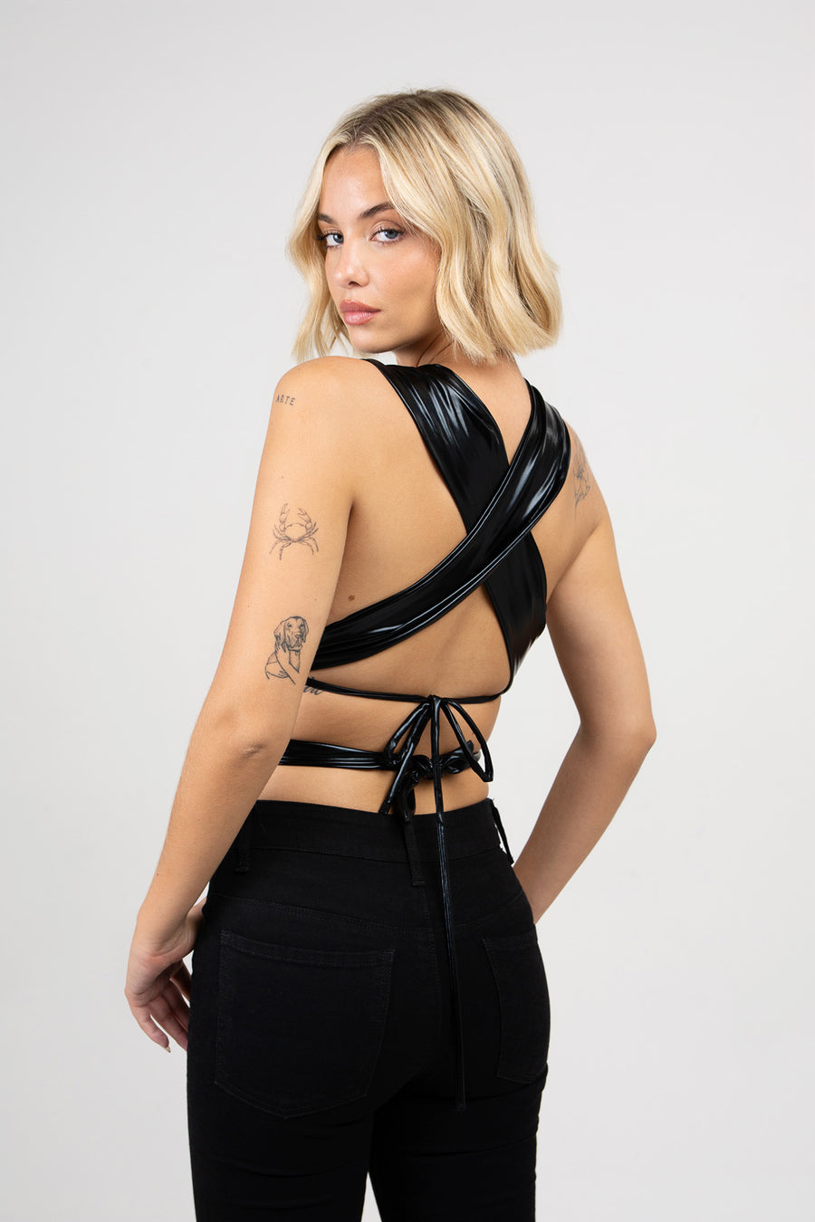 Modelo posando de espaldas con Top Doll triángulo de spandex metalizado con distintas variantes de uso.