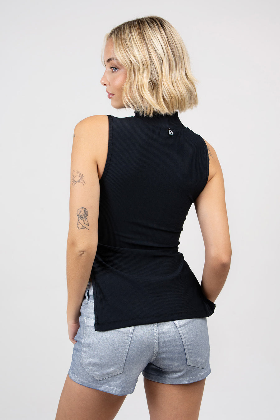 Modelo posando de espaldas usando Top Lucius ajustado sin mangas con recortes en el lateral.