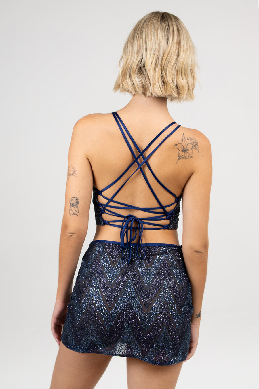 Mujer posando de espaldas con Top Wren traslúcido con cuello halter y espalda descubierta con breteles trenzados.